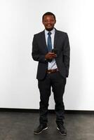 sorridente africano americano Preto homem dentro o negócio terno com Smartphone branco parede fundo foto