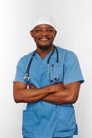 sorridente cirurgião negro médico barbudo homem de casaco azul e boné médico com estetoscópio braços cruzados foto