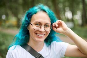 jovem adulto mulher retrato dentro volta óculos com turquesa tingido cabelo em verde floresta fundo foto