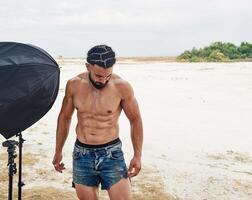 jovem muscular homem exercício em a praia, jovem muscular homem fazendo musculação exercícios em a praia, Atlético jovem homem em a de praia foto