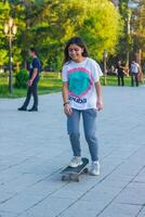 jovem menina jogando em a Parque infantil, menina com skate, jovem menina em skate dentro a parque foto