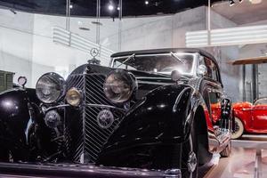 estugarda, alemanha - 16 de outubro de 2018 museu mercedes. veículo vermelho atrás. carro retro preto polido com roda sobressalente estacionado dentro de casa foto