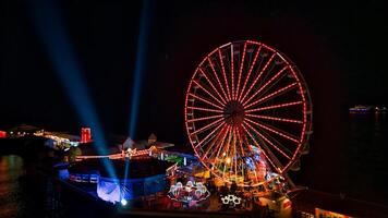 iluminado ferris roda às noite com vibrante luzes e feixes contra uma Sombrio céu. foto