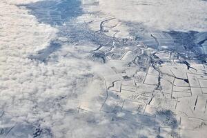 vista aérea sobre o topo das nuvens para rios cobertos de neve, campos e estradas, ar fresco gelado de inverno foto