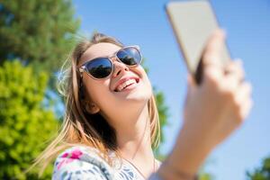 ai gerado menina dentro oculos de sol leva uma selfie com uma Smartphone em a cidade rua foto