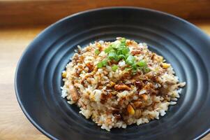 frito arroz com carne de porco e cogumelos dentro Preto prato em de madeira mesa foto