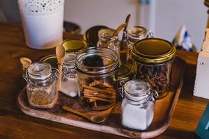 especiarias e ervas dentro vidro frascos em uma de madeira mesa dentro a cozinha foto