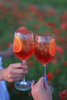 dois óculos do vermelho vinho com gelo e laranja em a papoula campo foto