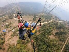 parapente dentro a montanhas, a dois pessoas em a topo do a montanha, a pára-quedistas estão vôo com uma pára-quedas foto