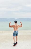 jovem muscular homem exercício em a praia, jovem muscular homem fazendo musculação exercícios em a praia, Atlético jovem homem em a de praia foto