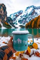 ai gerado mão segurando uma caneca com Nevado montanha pano de fundo dentro outono foto