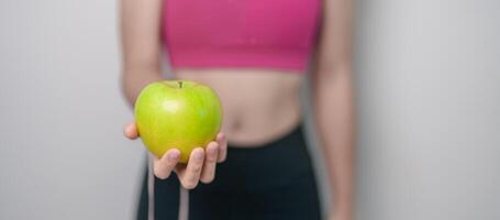 mulher mão aguarde verde maçã, feliz fêmea ginástica escolher fruta é saudável Comida. dieta ao controle, peso perda, obesidade, comendo estilo de vida e nutrição conceitos foto