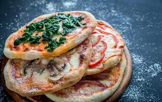 mini pizzas com várias coberturas na placa de madeira foto