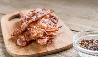 pilha do frito bacon tiras em a de madeira borda foto