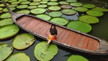 menina sentado em uma grandes rabo barco cercado de rainha victoria água lírios dentro phuket Tailândia foto