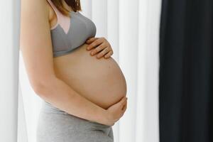 jovem grávida mulher detém dela mãos em dela inchado barriga. amor conceito. horizontal com cópia de espaço foto