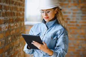 absorvido dentro a trabalhos do uma mulher engenheiro trabalhando com uma tábua em a fundo do a construção local. retrato do uma jovem arquiteto, protetora equipamento. seletivo foco foto