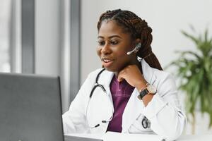 africano americano mulher médico trabalhando às dela escritório conectados usando portátil informação dispositivo. telemedicina Serviços. primário Cuidado consultas, psicoterapia, emergência Serviços foto