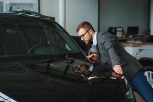 visitando carro concessionária. bonito barbudo homem é acariciando dele Novo carro e sorridente foto