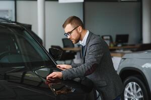 visitando carro concessionária. bonito barbudo homem é acariciando dele Novo carro e sorridente foto