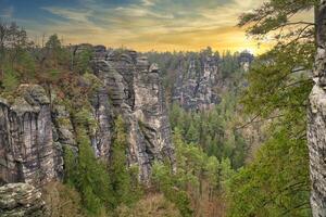 áspero pedras às Basteibridge às pôr do sol. Largo Visão sobre árvores e montanhas foto