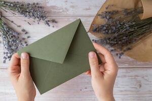 plano deitar composição do fêmea mãos segurando verde envelope com seco lavanda flores cópia de espaço modelo zombar acima. topo visualizar. conceito do Casamento convite cartão postal. o negócio propaganda marca em branco foto