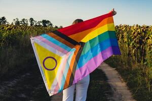 jovem mulher corre dentro campo com arco Iris LGBTQIA bandeira acenando dentro vento fez a partir de seda material em campo fundo. símbolo do lgbtq orgulho mês. igual direitos. Paz e liberdade conceito foto