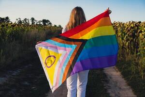 símbolo do lgbtq orgulho mês. jovem mulher mostrando arco Iris LGBTQIA bandeira acenando dentro vento fez a partir de seda material em campo fundo. igual direitos. Paz e liberdade conceito foto