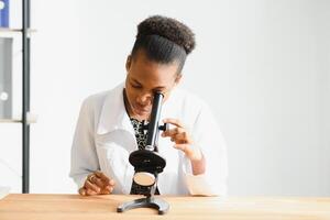 africano americano fêmea laboratório técnico olhando através microscópio dentro laboratório. foto