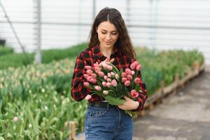 lindo jovem sorridente garota, trabalhador com flores dentro estufa. conceito trabalhos dentro a estufa, flores foto