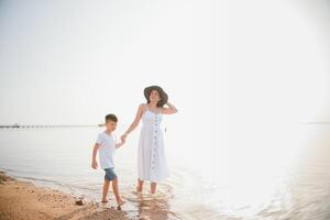 feliz mãe com filho andar em praia, família às mar foto