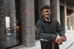 jovem africano americano cara com elétrico lambreta dentro a cidade. a conceito do ecológico transporte. foto