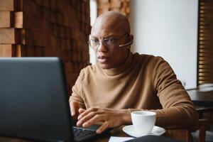 focado africano homem vestindo fones de ouvido assistindo webinar Treinamento fazer notas estude conectados Aprendendo língua em computador, Preto masculino aluna olhando às computador portátil elearning dentro Internet escrever Informação. foto