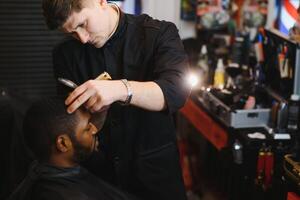 retrato do jovem Preto homem ser aparado com profissional elétrico tosquiadeira máquina dentro barbearia.masculino beleza tratamento conceito. jovem africano cara obtendo Novo corte de cabelo dentro barbeiro salão foto