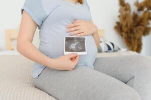 grávida mulher é segurando dela estômago e uma foto do dela ultrassom