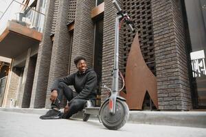 jovem africano americano cara com elétrico lambreta dentro a cidade. a conceito do ecológico transporte. foto