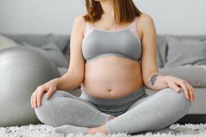 fechar-se tiro do irreconhecível grávida mulher meditando às lar, expectante senhora sentado dentro lótus posição com apertado mãos, praticando ioga para saudável gravidez, cortada imagem com livre espaço foto
