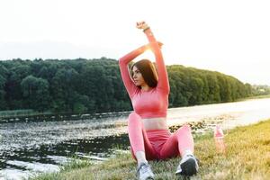 jovem caucasiano mulher fazendo ativo Treinamento exercício em uma ioga esteira perto a rio dentro verão. conceito do saudável estilo de vida foto