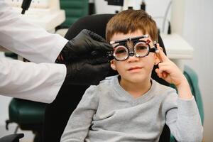 pequeno sério Garoto sentado em cadeira escritório do visão teste. médico picaretas acima lentes para especial óculos. foto