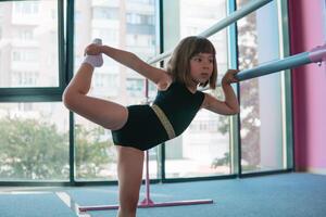 lindo menina ginasta dentro uma Preto malha fazendo alongamento exercícios. Esportes clube para meninas foto