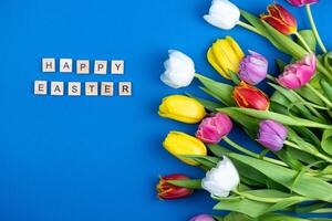 ramalhete do multicolorido tulipas em uma azul fundo. feliz Páscoa frase. Primavera flor. festivo cumprimento cartão. flores topo visualizar. cópia de espaço foto