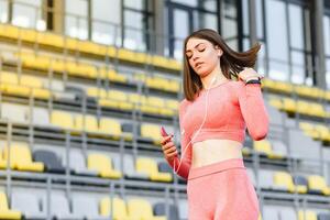 jovem atraente ginástica modelo ouvindo música em inteligente telefone queimando positivo energia antes exercite-se fora. foto