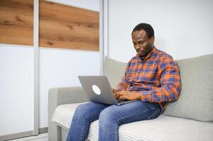 conectando com a conectados mundo. tiro do uma feliz jovem homem usando uma computador portátil enquanto relaxante às casa foto