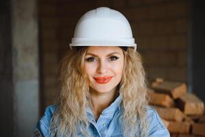 atraente fêmea construção trabalhador dentro capacete. confiante jovem especialista dentro xadrez azul camisa dentro jeans em pé dentro esvaziar sala. interior Projeto e renovação serviço foto