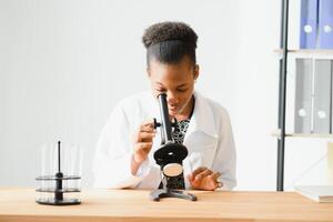 africano americano fêmea laboratório técnico olhando através microscópio dentro laboratório. foto
