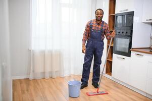 jovem africano homem lavagens a chão com uma esfregão dentro a quarto foto