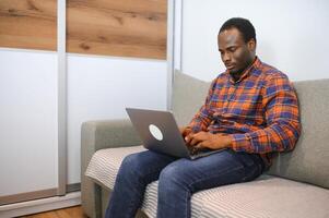 conectando com a conectados mundo. tiro do uma feliz jovem homem usando uma computador portátil enquanto relaxante às casa foto