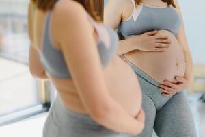 lindo grávida mulher em pé perto espelho às casa foto