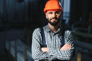 feliz profissional pesado indústria engenheiro trabalhador vestindo uniforme, e Difícil chapéu dentro uma aço fábrica. sorridente industrial especialista em pé dentro uma metal construção fabricação foto