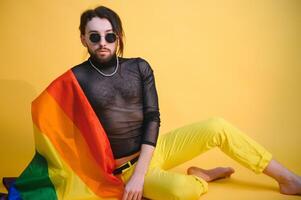 gay homem com uma gay orgulho bandeira sorridente e olhando longe em amarelo fundo foto